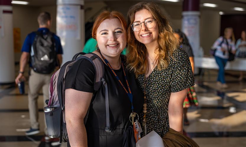Two women wearing dark shirts smile in the hallway of a school